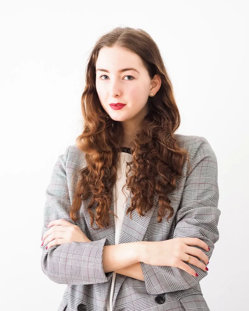 A woman with long wavy auburn hair in a grey checked blazer