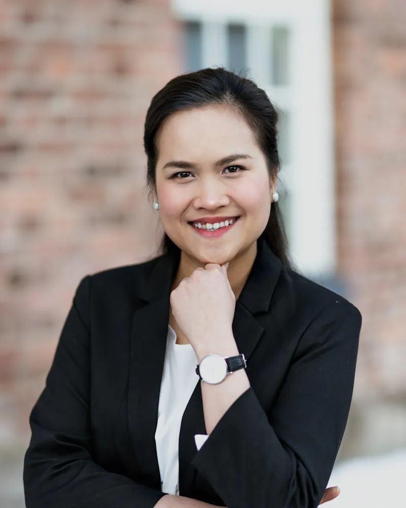 A smiling woman in a black blazer with her hand at her chin