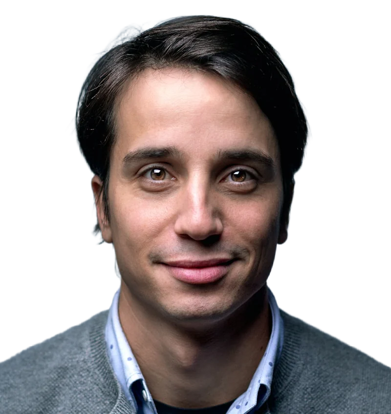 A man with dark hair and a calm expression in a grey knit sweater