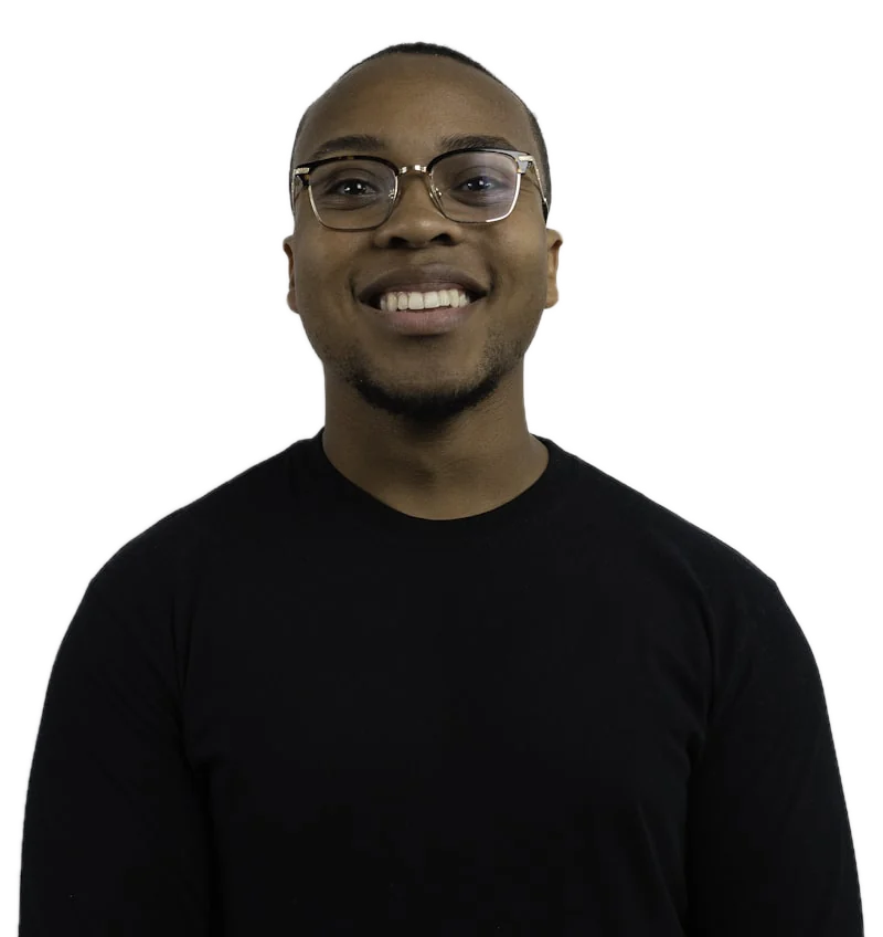 A smiling man in glasses and a black sweater against a white wall