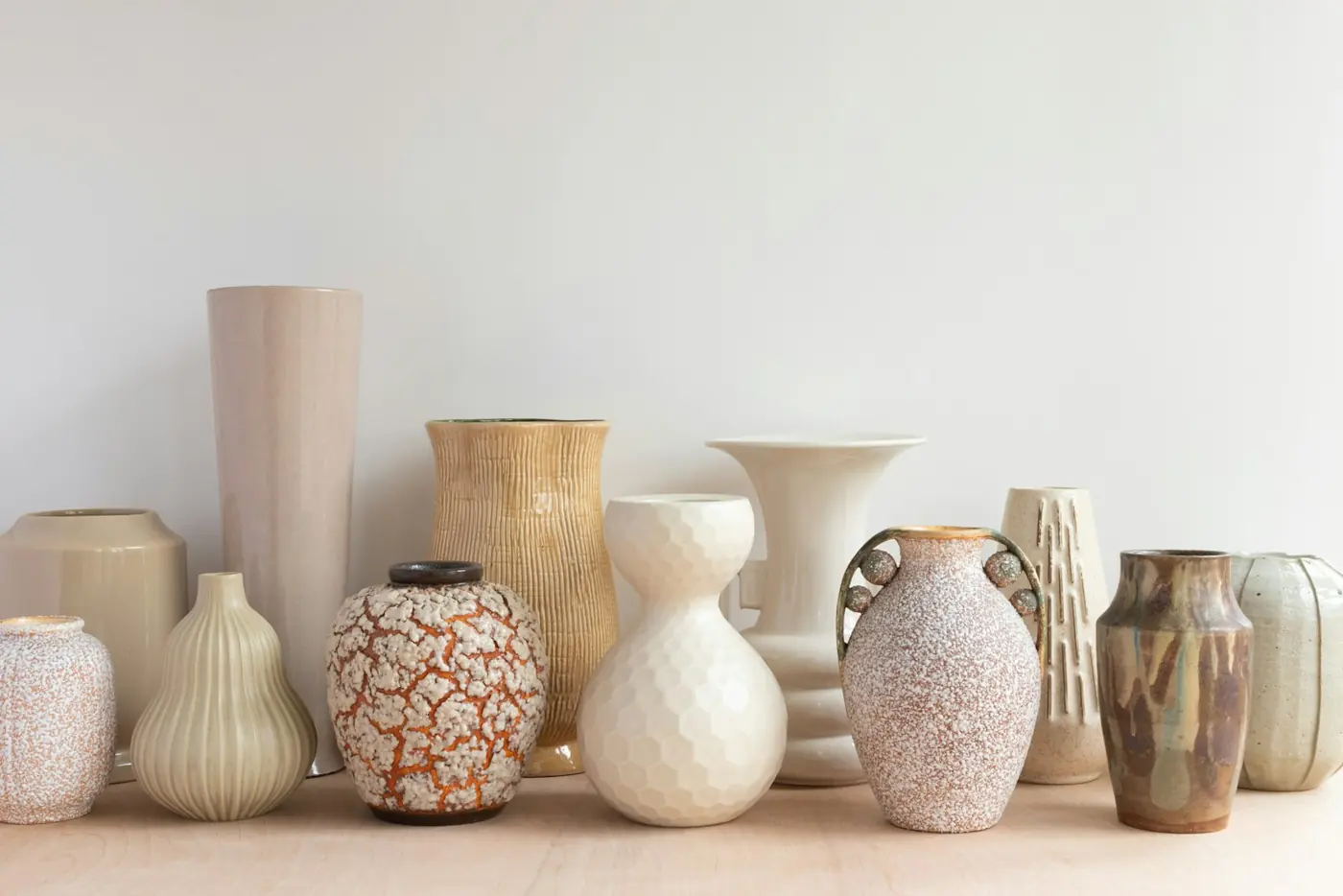 A row of ceramic vases on a shelf against a white wall