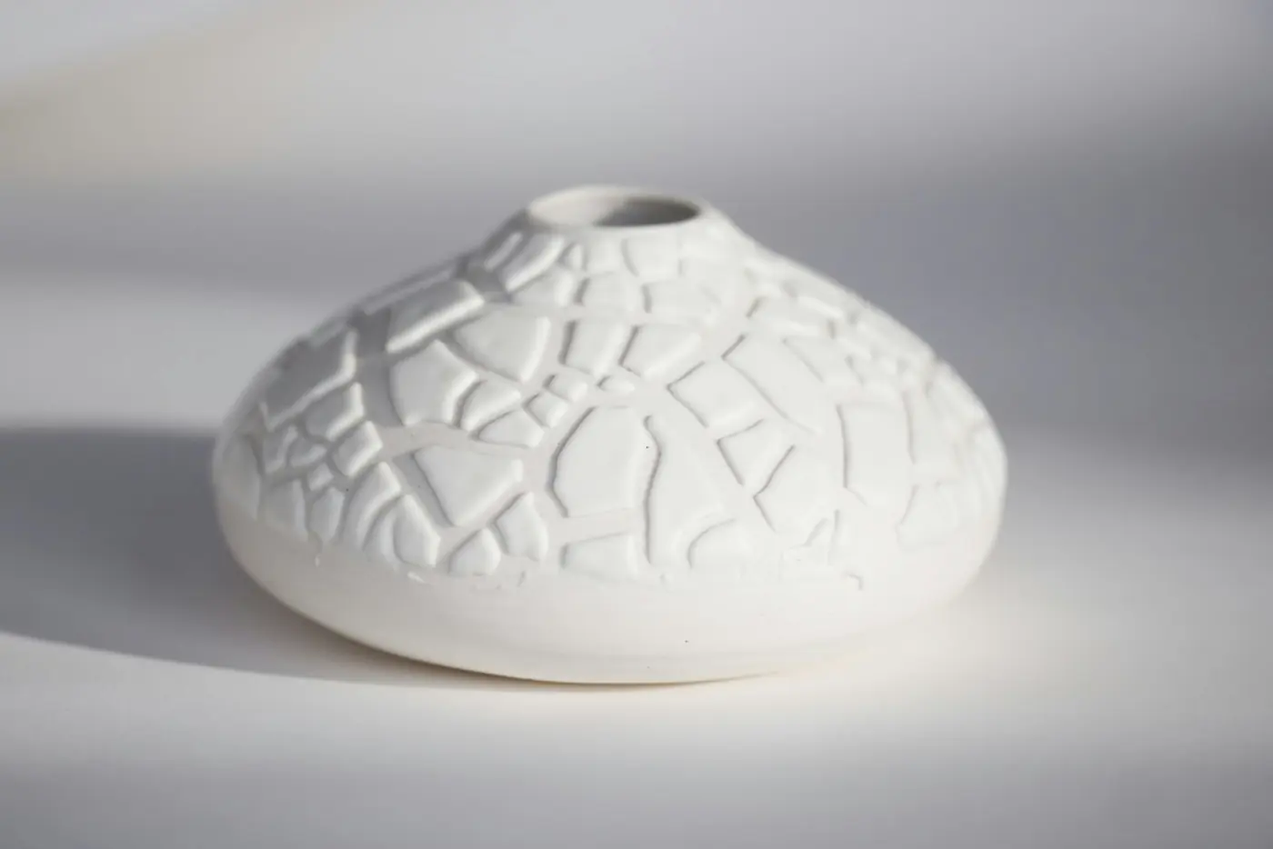 A white vase with a cracked-tile texture on a pale surface